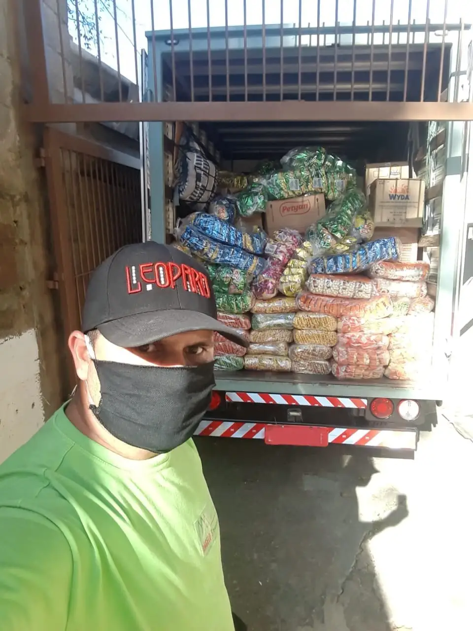 Homem de camisa verde da Angelos Transportes e caminhão carregado de caixas e produtos para entrega